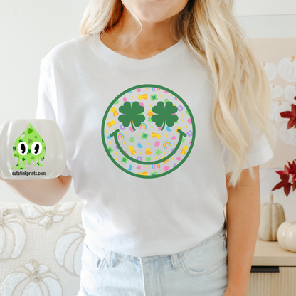 A person wearing a white t-shirt with a graphic of a smiley face surrounded by a rainbow checkered pattern and clover leaves.