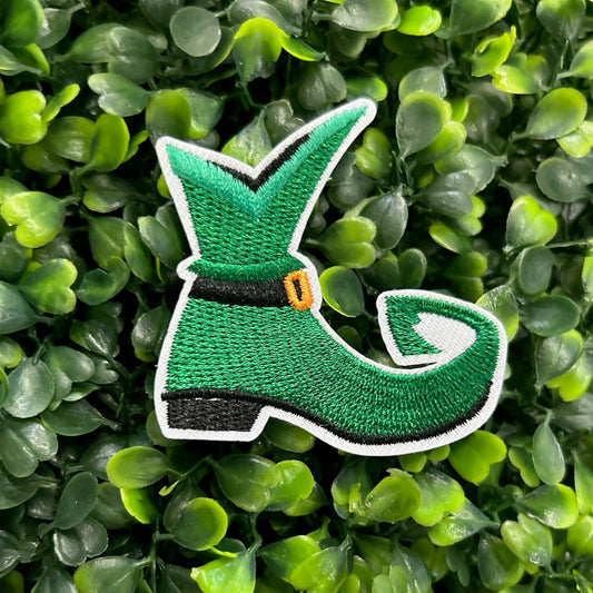 Green elf shoe embroidered patch with curled toe, buckle, and white border.