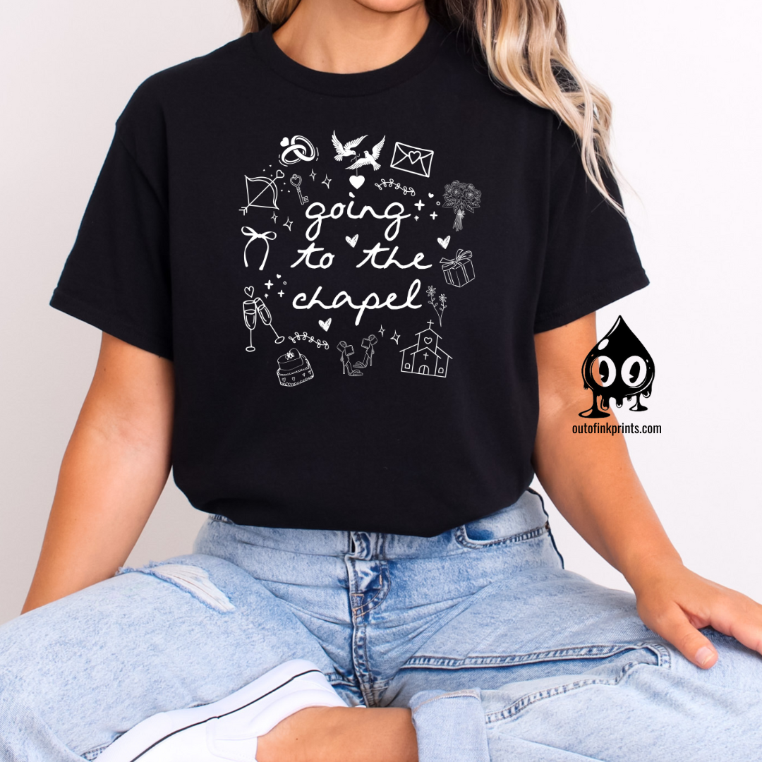A woman sitting and wearing a black T-shirt with white text that reads 'Going to the Chapel' along with various symbols and text related to weddings.