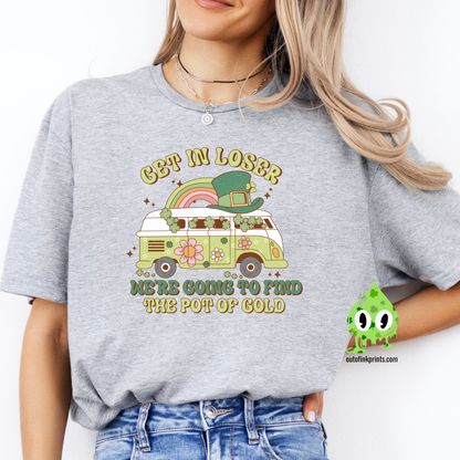 A woman wearing a gray t-shirt with the text 'GET IN LOSER ST. PATRICK'S' and a graphic of a pot of gold and a leprechaun.
