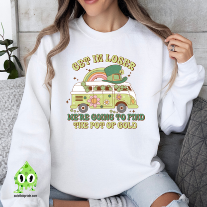 A woman wearing a white sweatshirt with a St. Patrick's Day theme, featuring text and a graphic of a rainbow, clover, and what appears to be a leprechaun.