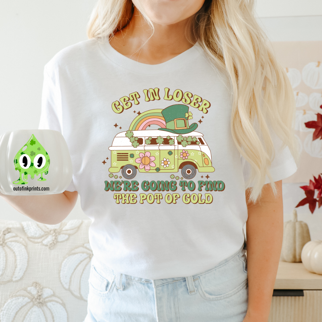 A woman wearing a white t-shirt with the text 'GET IN LOSER ST. PATRICK'S' and a graphic of a pot of gold and a leprechaun.