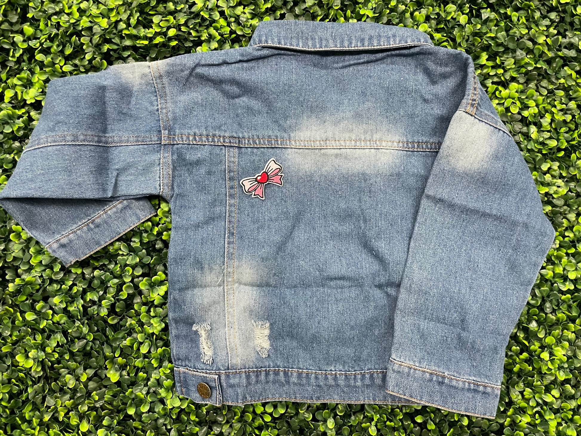 Blue jean jacket with a patch attached to the back that has a pink and white bowtie design with a heart in the center