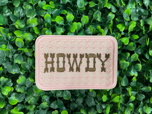 Patch with 'HOWDY' text on a pink background, placed on green leaves.