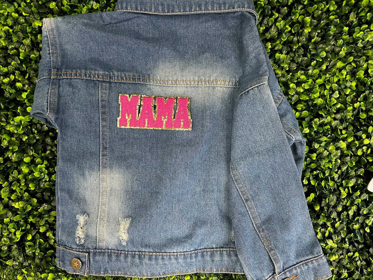 Blue denim jacket with pink text patch on a grass background