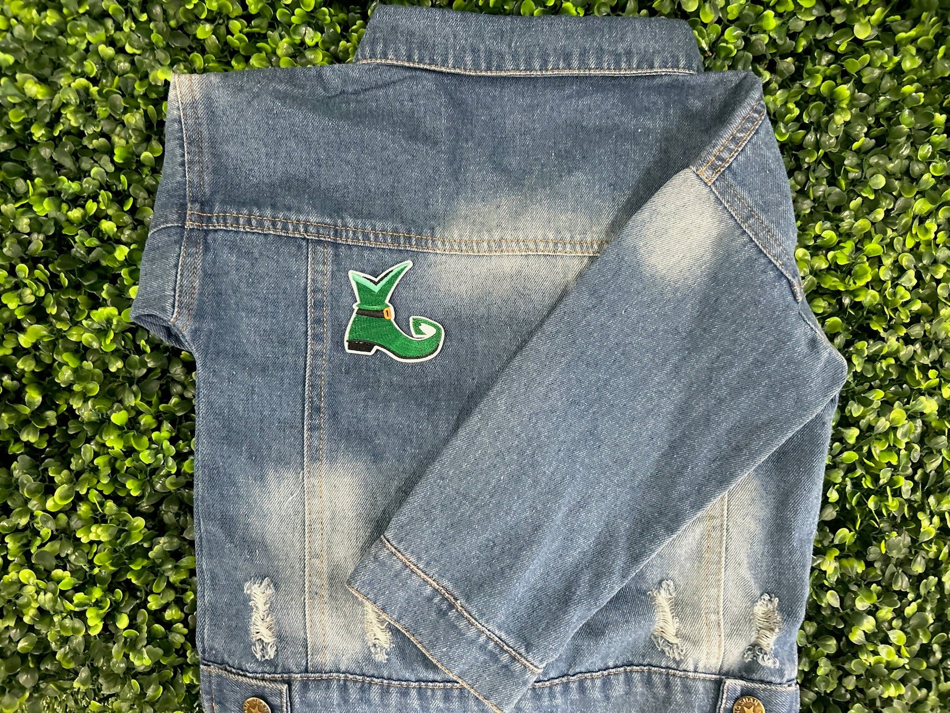 Green elf shoe embroidered patch with curled toe, buckle, and white border held on a children's jean jacket