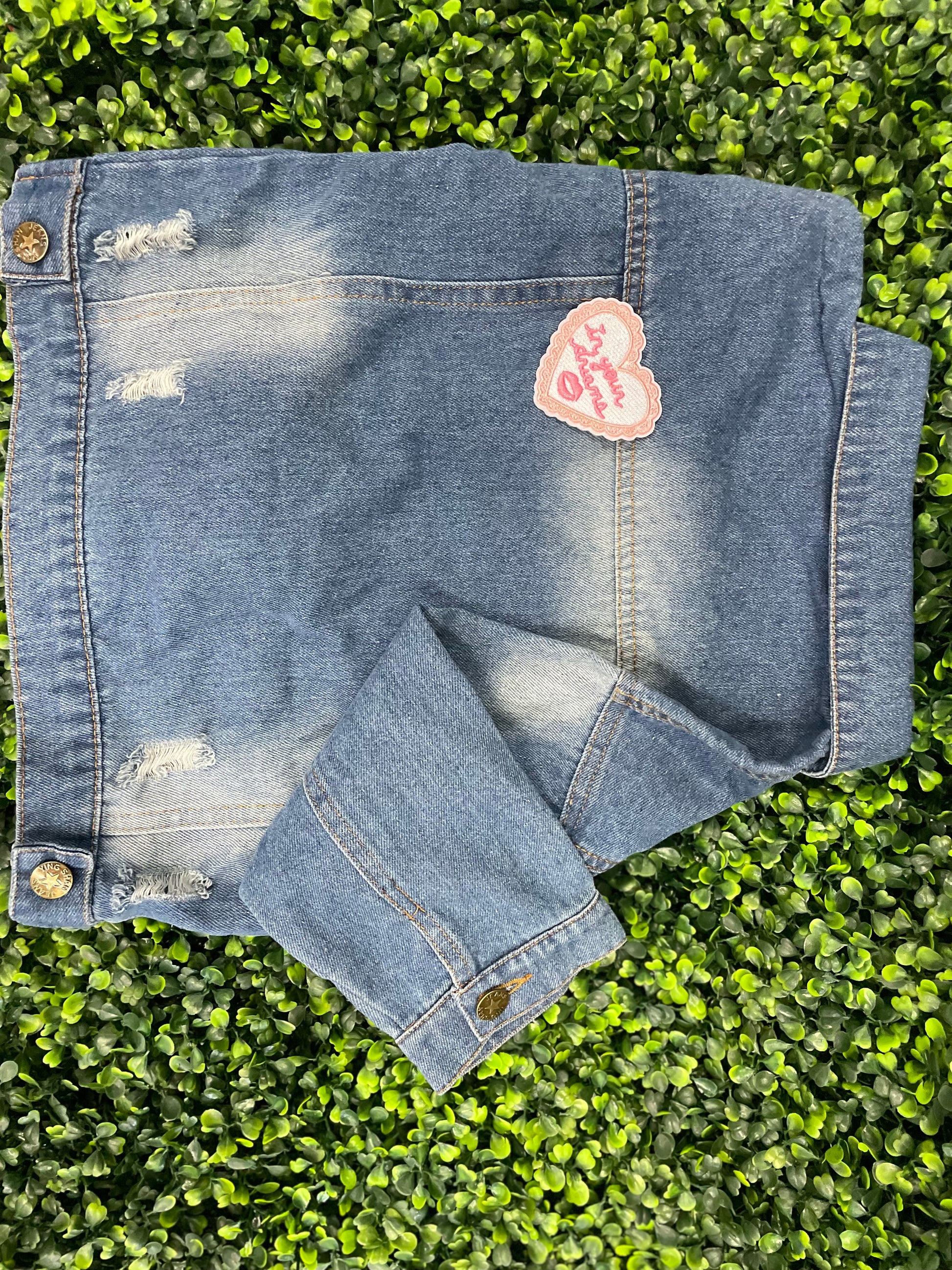 Heart-shaped embroidered patch with 'In your dreams' text held against a children's denim jean jacket