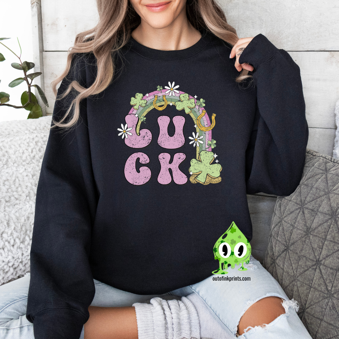 A woman wearing a black sweatshirt with the text 'LUCK' arranged in a playful design using Irish-themed graphics such as shamrocks and a four-leaf clover.