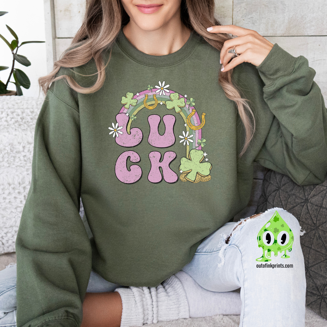 A woman wearing a green sweatshirt with the text 'LUCK' arranged in a playful design using Irish-themed graphics such as shamrocks and a four-leaf clover.