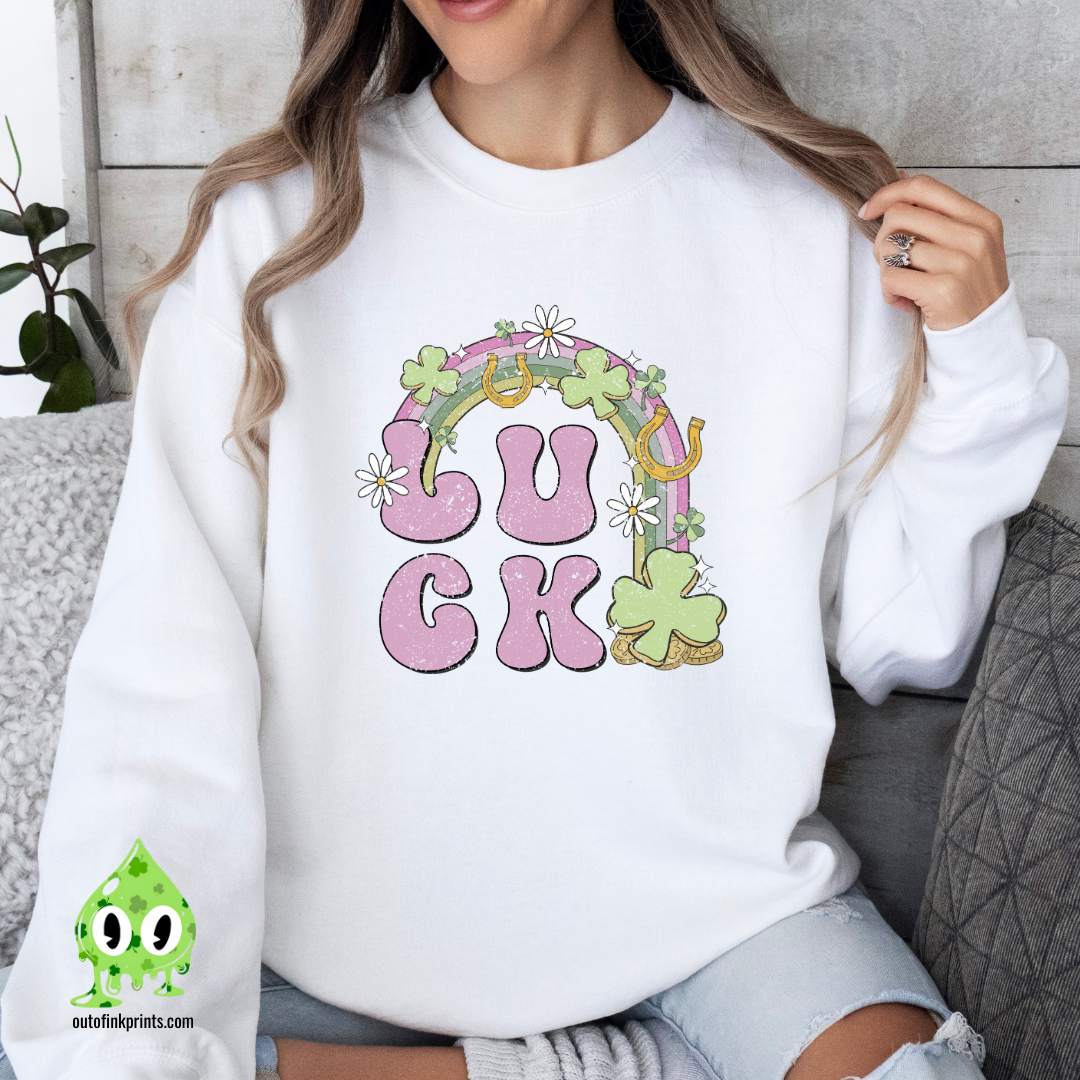 A woman wearing a white sweatshirt with the text 'LUCK' arranged in a playful design using Irish-themed graphics such as shamrocks and a four-leaf clover.
