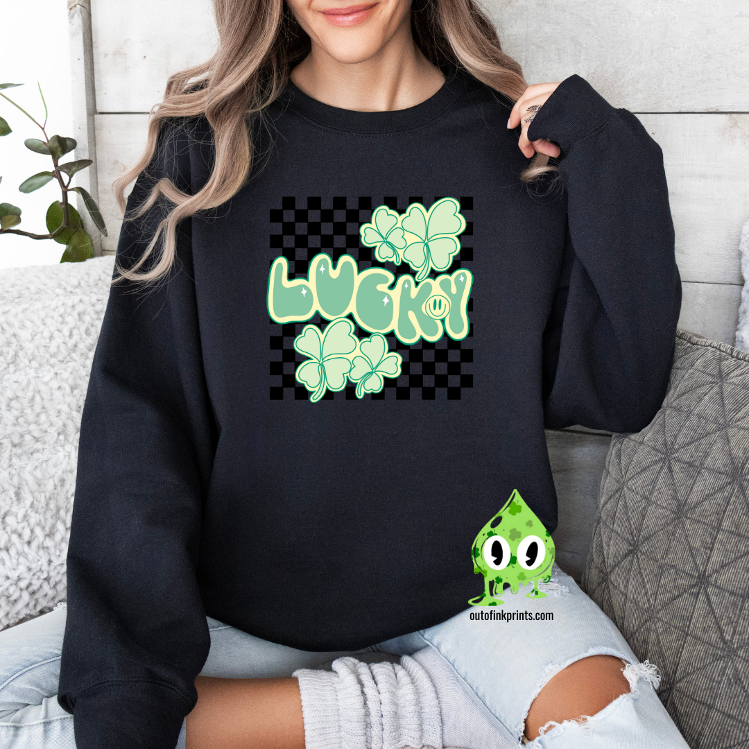 A woman wearing a black sweatshirt with a checkered pattern and a design that includes the text 'LUCKY' and shamrock shapes in a lighter green.