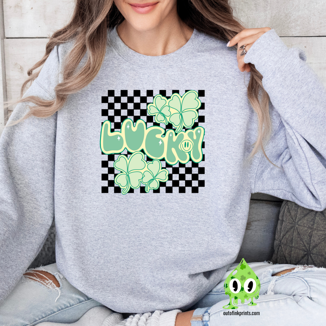 A woman wearing a grey sweatshirt with a checkered pattern and a design that includes the text 'LUCKY' and shamrock shapes in a lighter green.