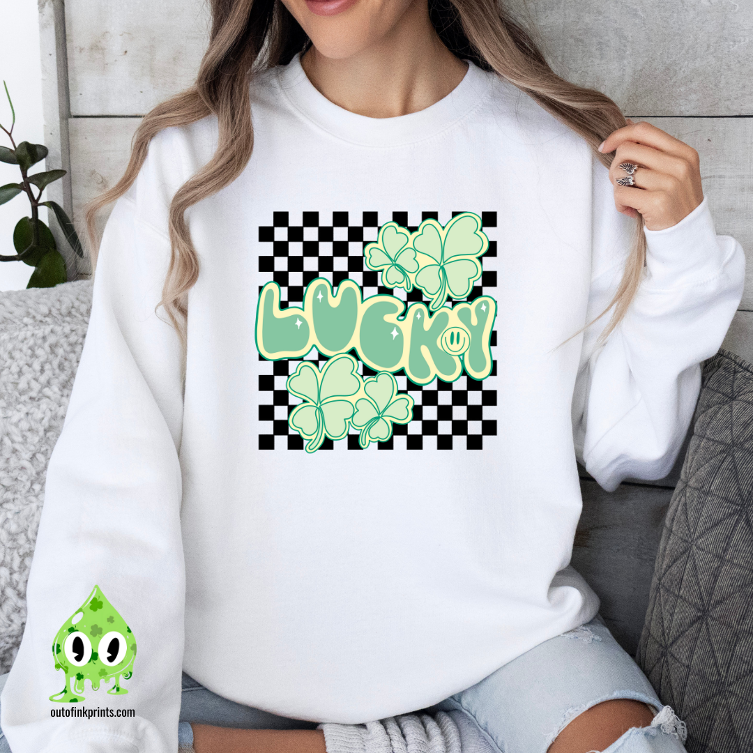 A woman wearing a white sweatshirt with a checkered pattern and a design that includes the text 'LUCKY' and shamrock shapes in a lighter green.