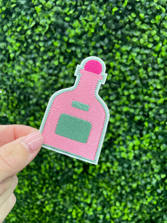 Pink bottle-shaped patch held against a green leafy background