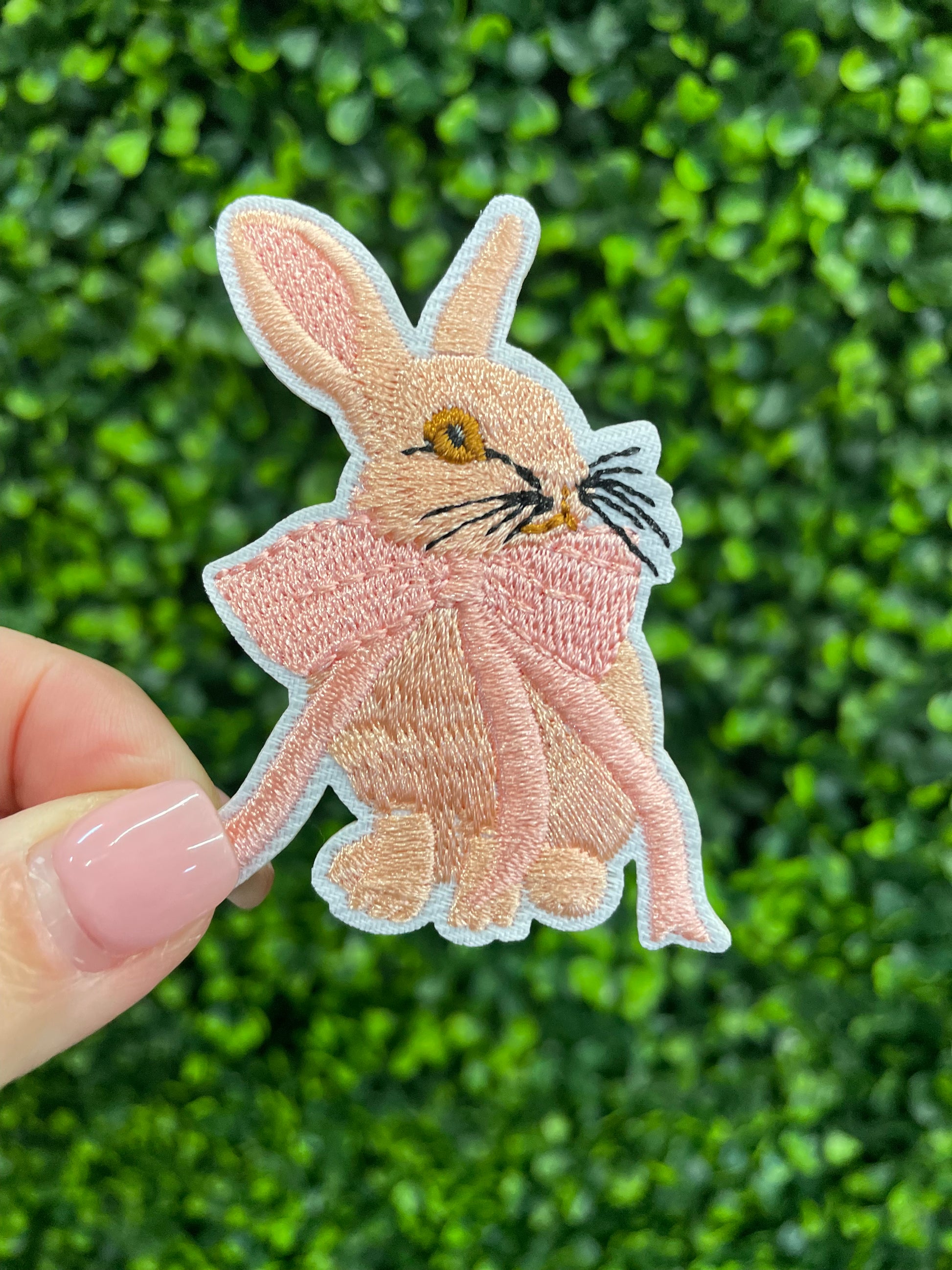 Embroidered patch of a pink bunny white a pink bow placed against a green leafy background