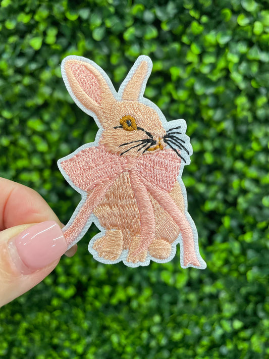 Embroidered patch of a pink bunny white a pink bow placed against a green leafy background