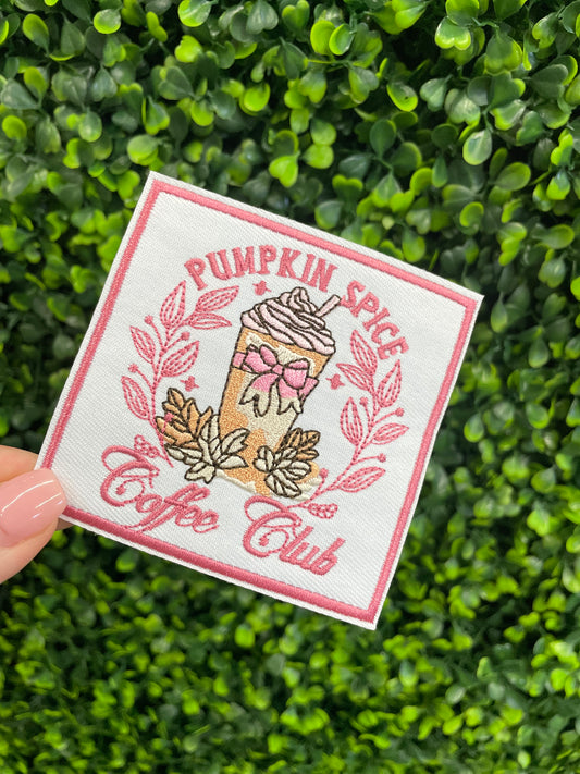 Sticker with pumpkin spice latte design and the text "pumpkin spice coffee club" held in front of green foliage