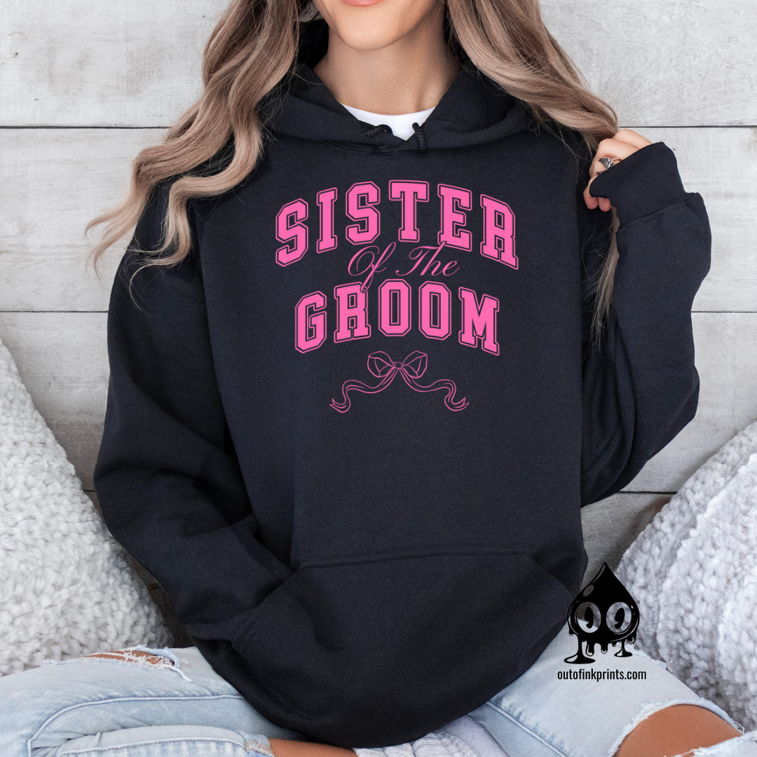 A woman wearing a black hoodie with 'Sister of the Groom' text and a pink bow design.