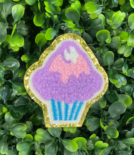 Decorative patch of a cupcake with pink and purple frosting, on a green leaf background