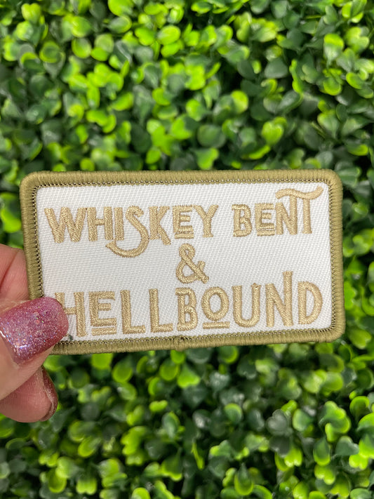 An embroidered patch with the text 'Whiskey Bent & Hellbound' held against a green leafy background.