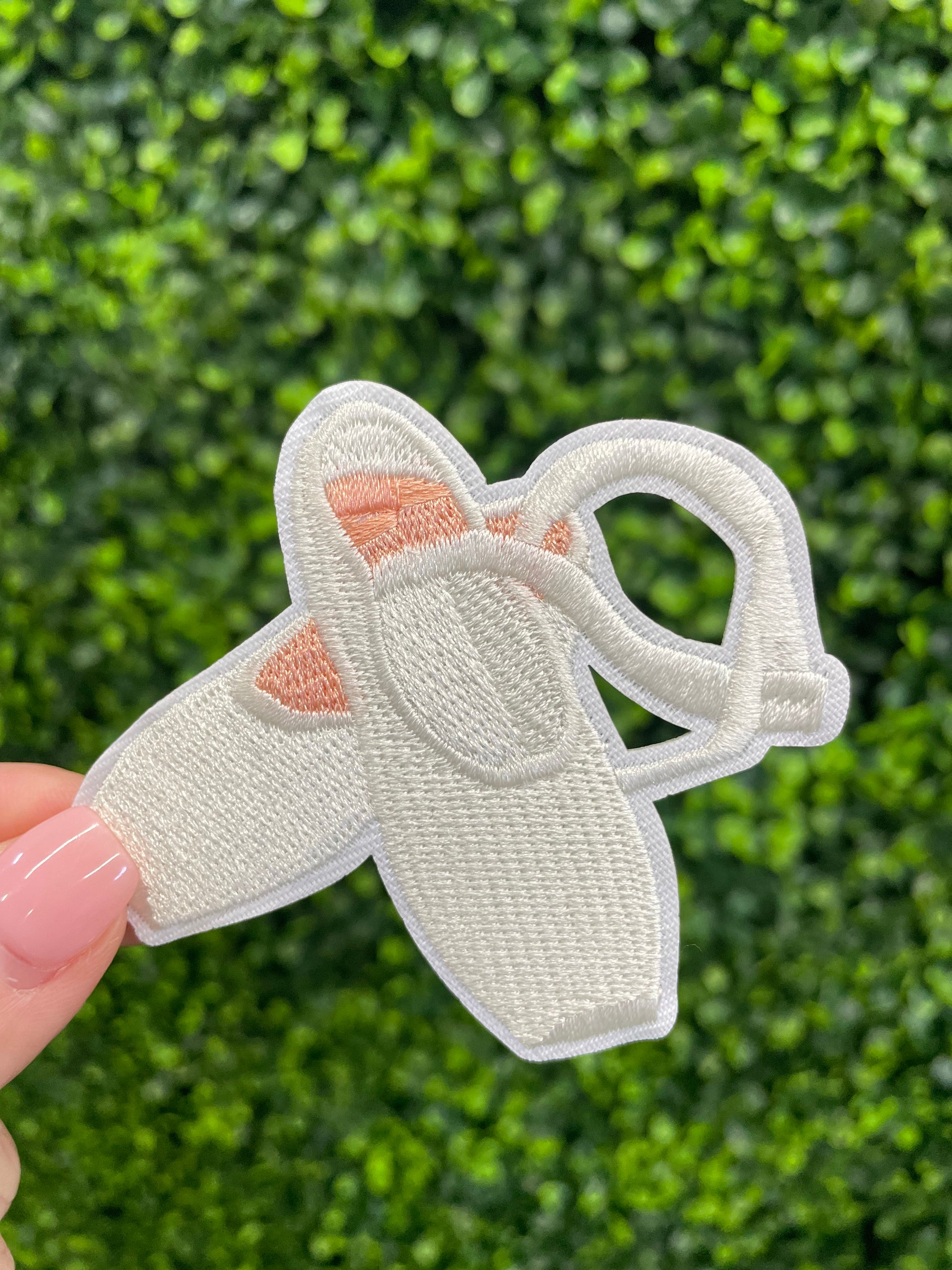 Embroidered patch of a pair of ballet slippers placed against a green leafy background