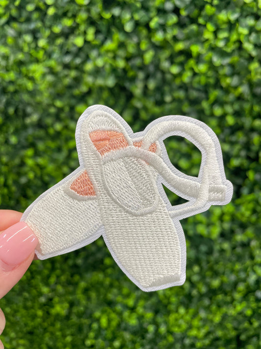 Embroidered patch of a pair of ballet slippers placed against a green leafy background