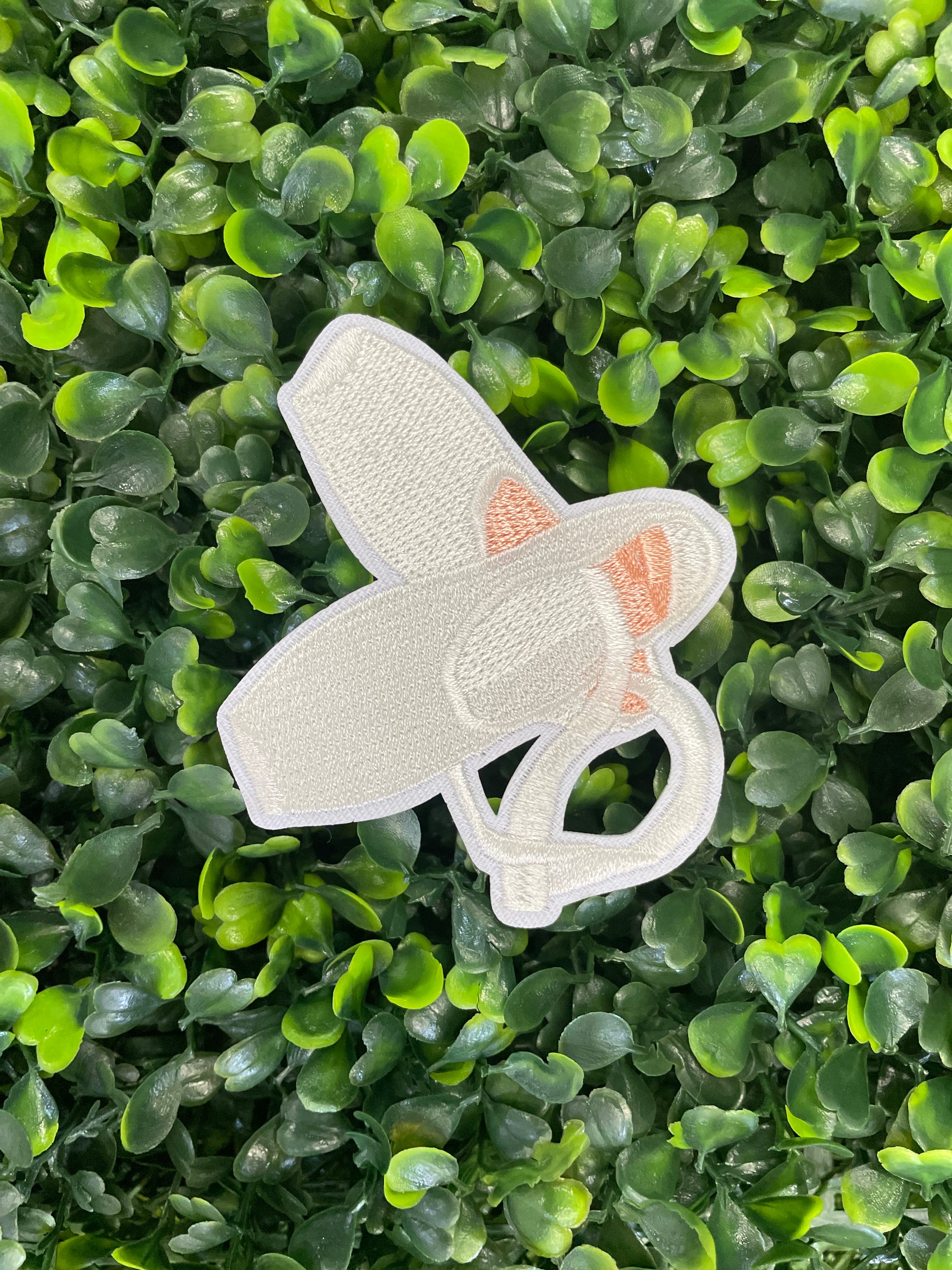 Embroidered patch of a pair of ballet slippers placed against a green and leafy background