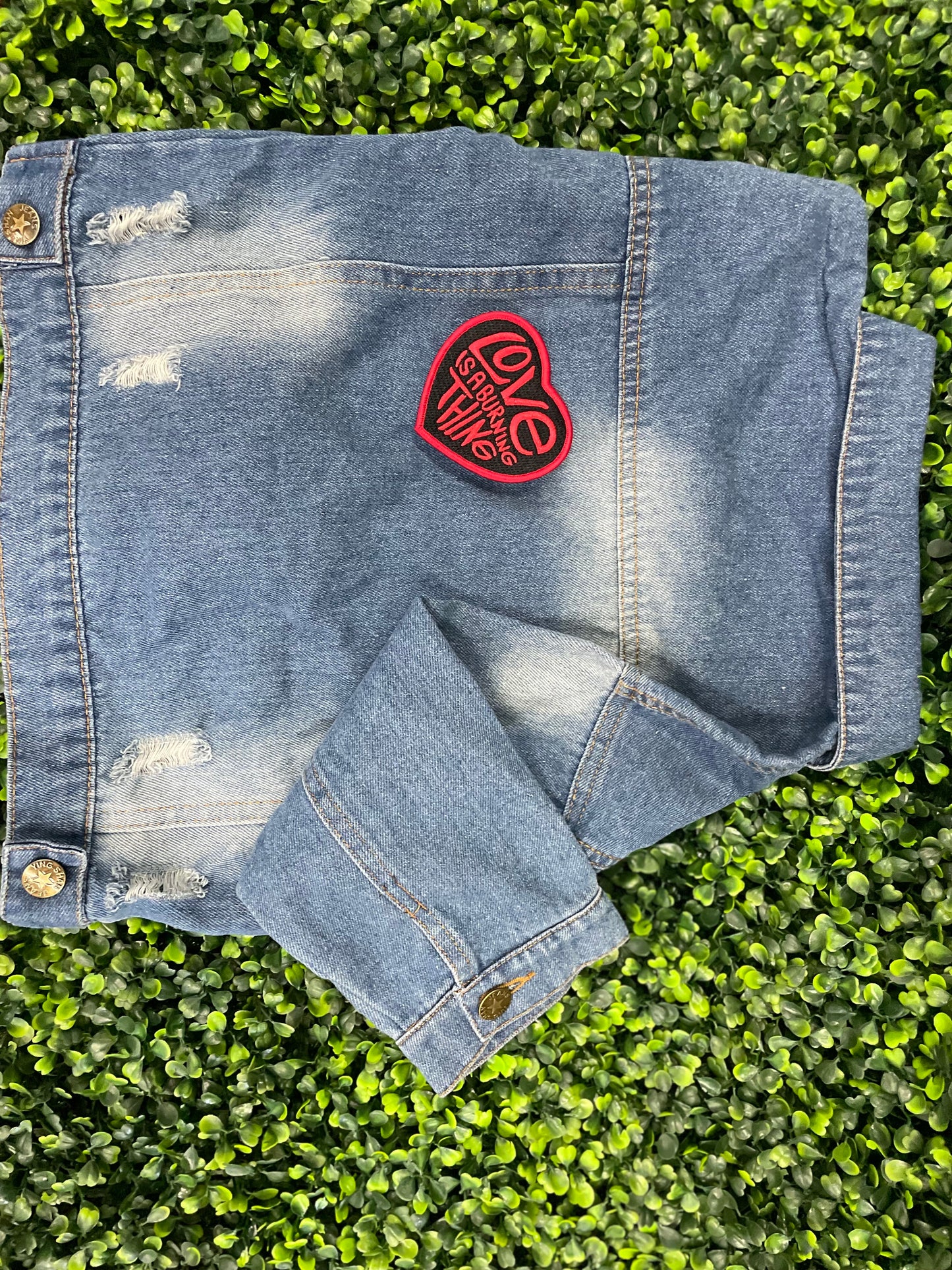 Heart-shaped patch with 'Love is a Burning Thing' text, placed on a children's denim jean jacket