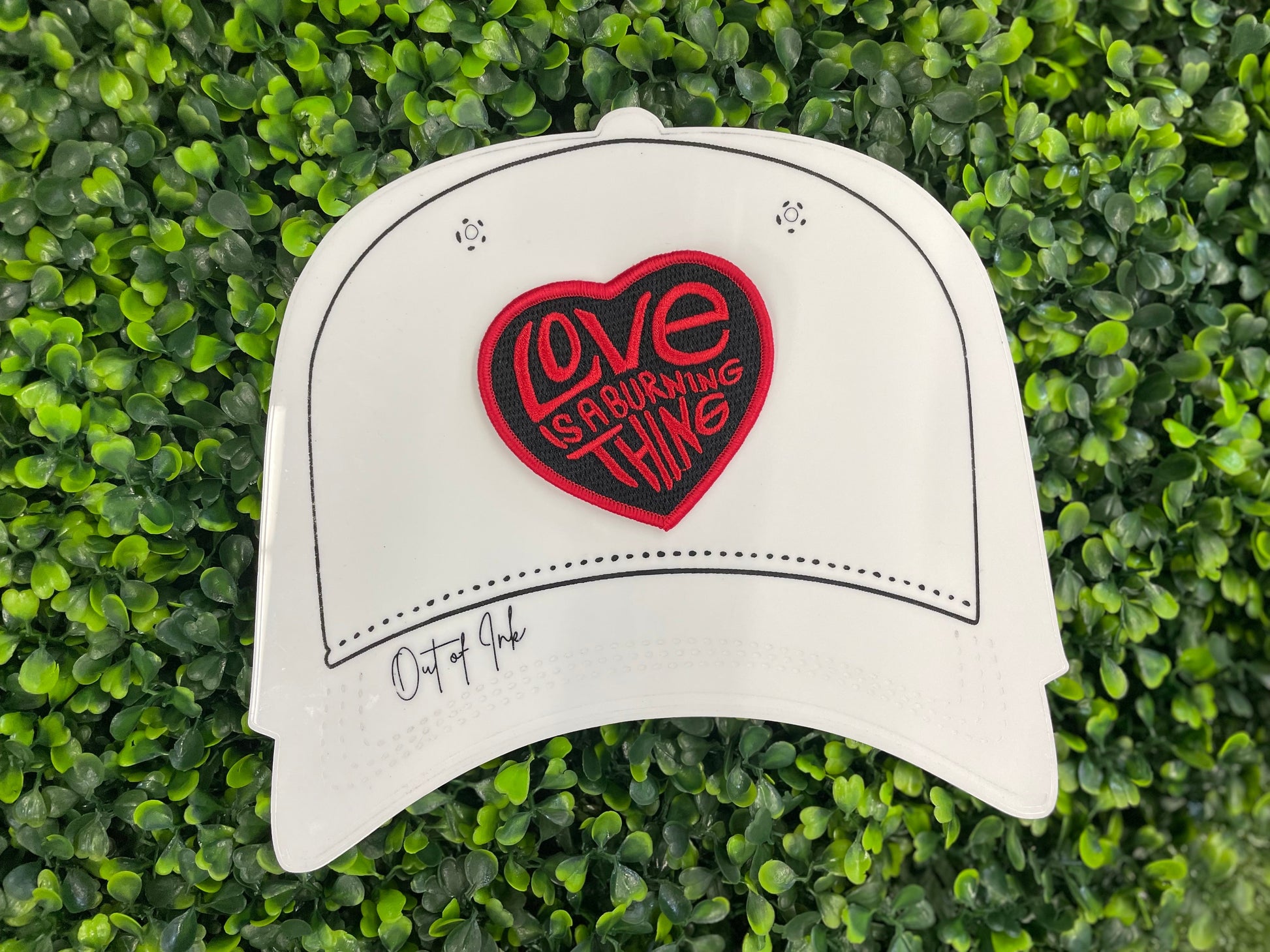 Heart-shaped patch with 'Love is a Burning Thing' text, placed on a white trucker hat