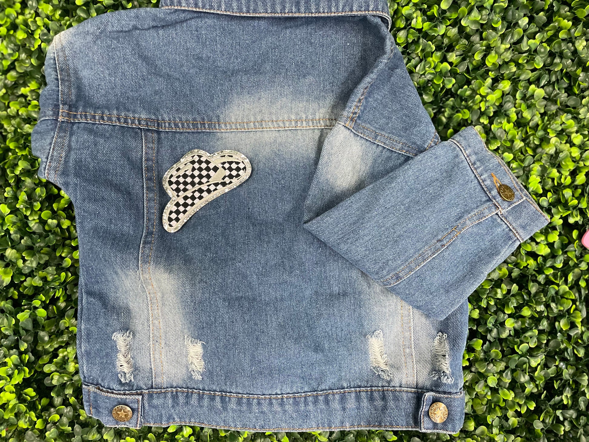 Checkered white and black cowboy hat patch with silver lining, placed onto a children's denim jean jacket