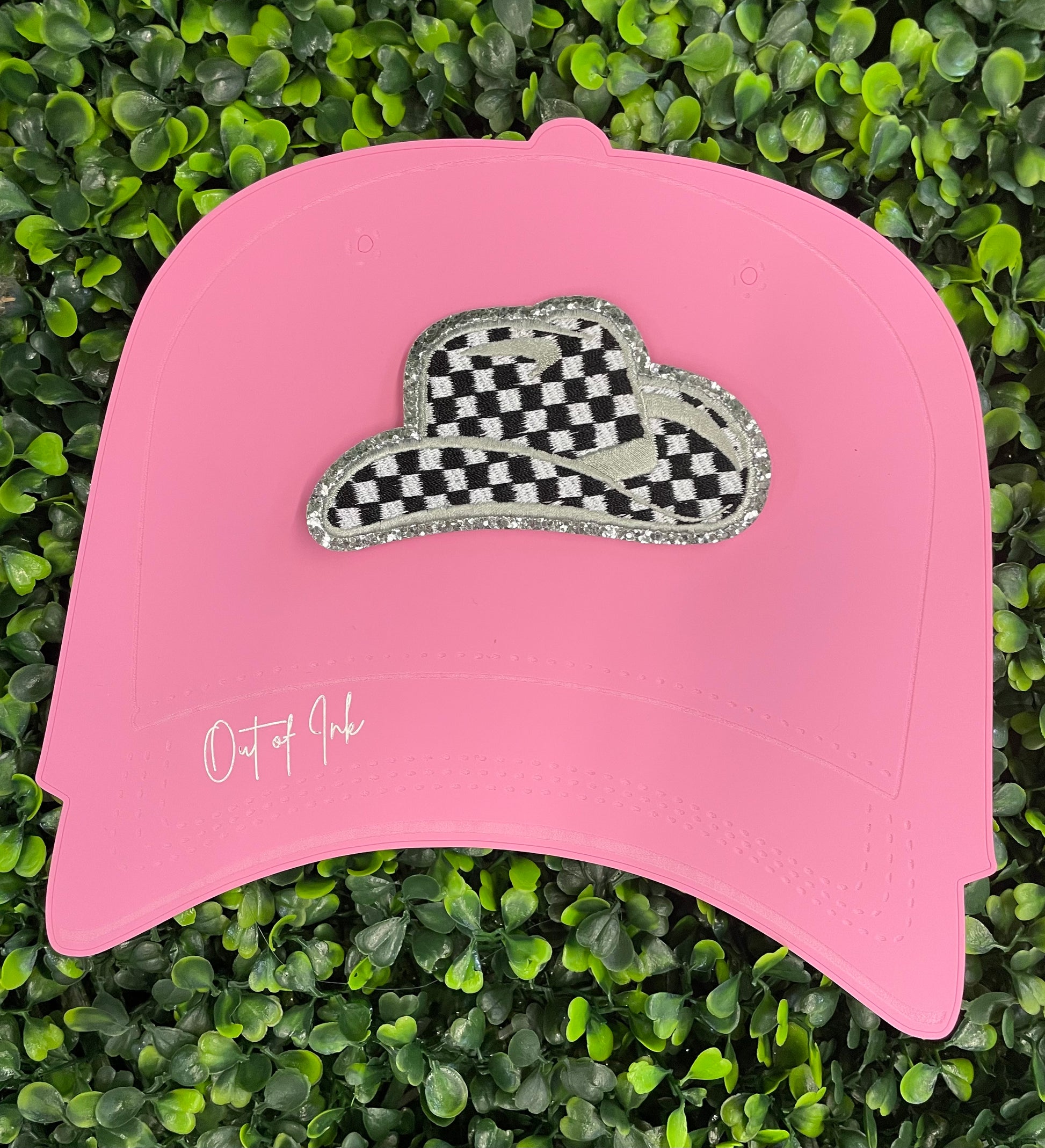 Checkered white and black cowboy hat patch with silver lining, placed onto a pink trucker hat graphic