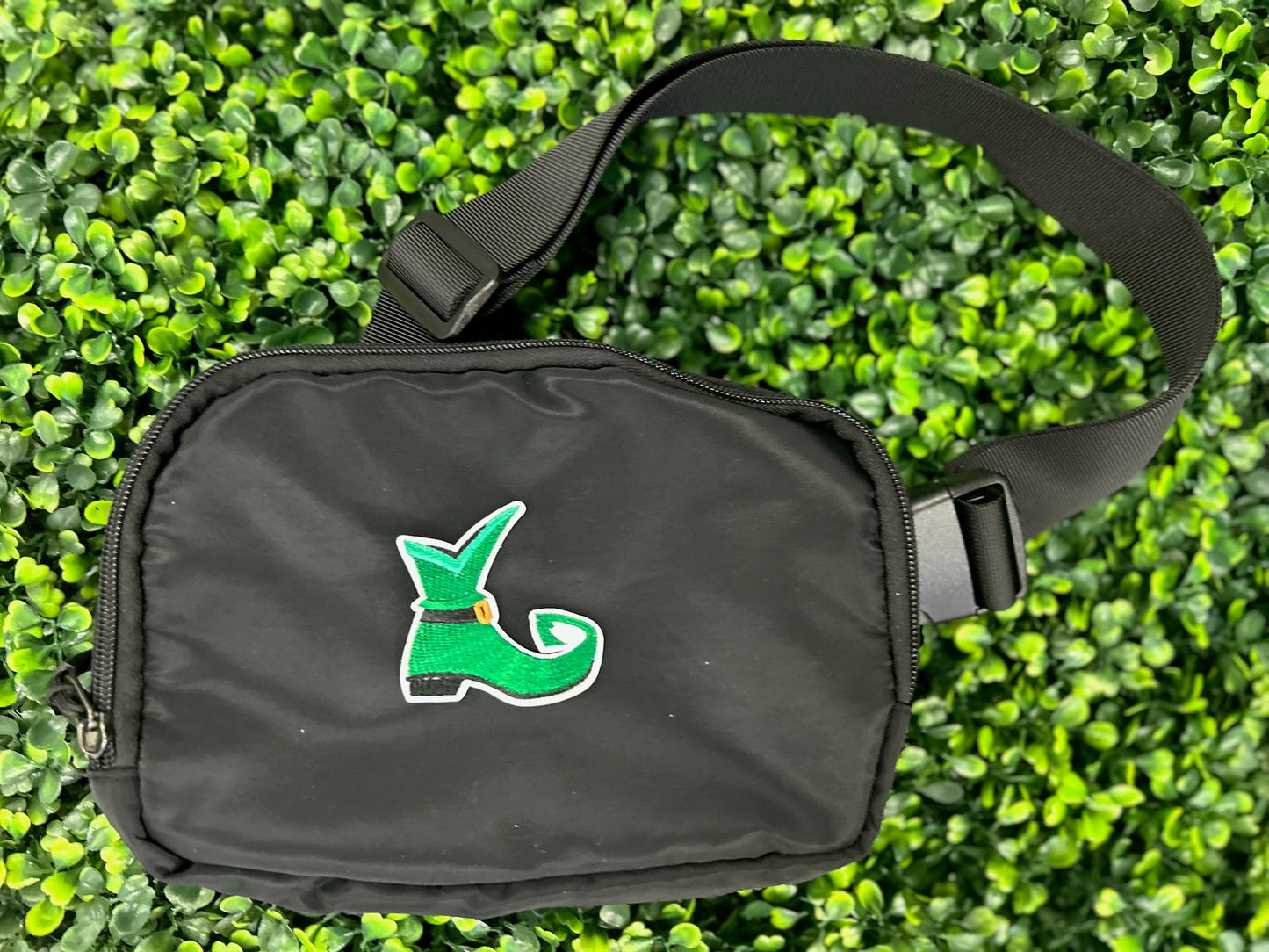 Green elf shoe embroidered patch with curled toe, buckle, and white border held on a black bag