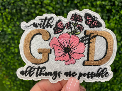 Embroidered patch butterflies and flowers and text stating "with God all things are possible", held against a green leafy background