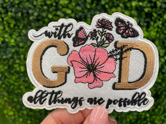 Embroidered patch butterflies and flowers and text stating "with God all things are possible", held against a green leafy background