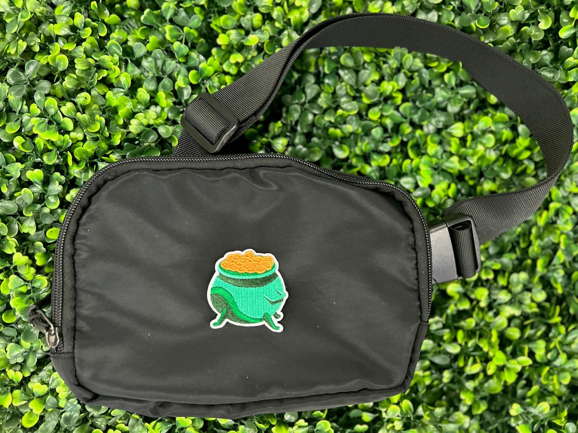 Green cauldron embroidered patch filled with gold coins and white border held on a black bag
