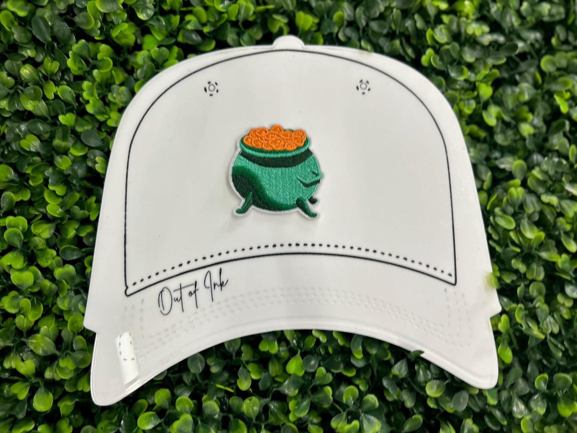 Green cauldron embroidered patch filled with gold coins and white border held on a white graphic hat