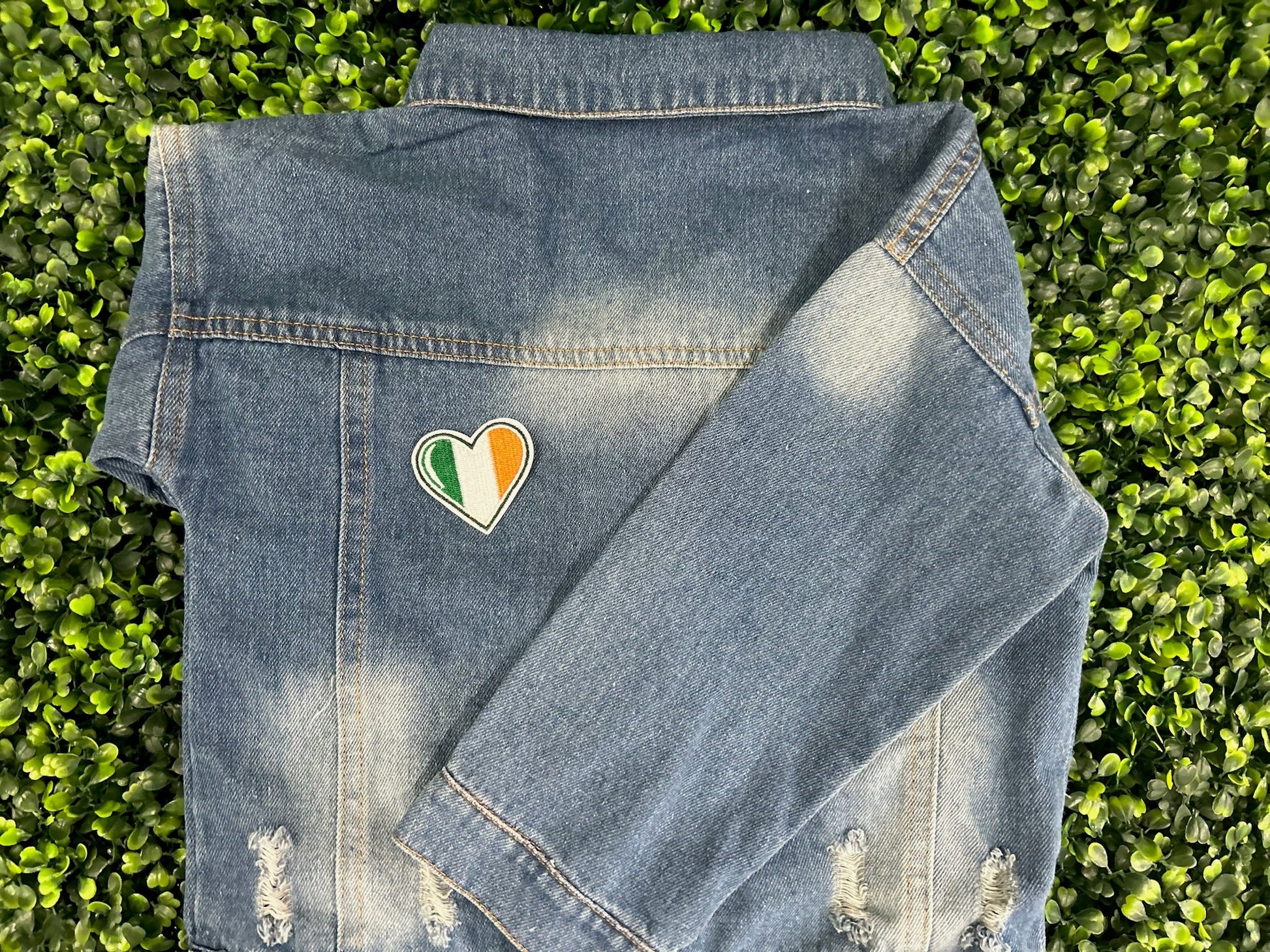 Heart shaped embroidered patch with Ireland flag colors green white and orange held on a children's denim jacket