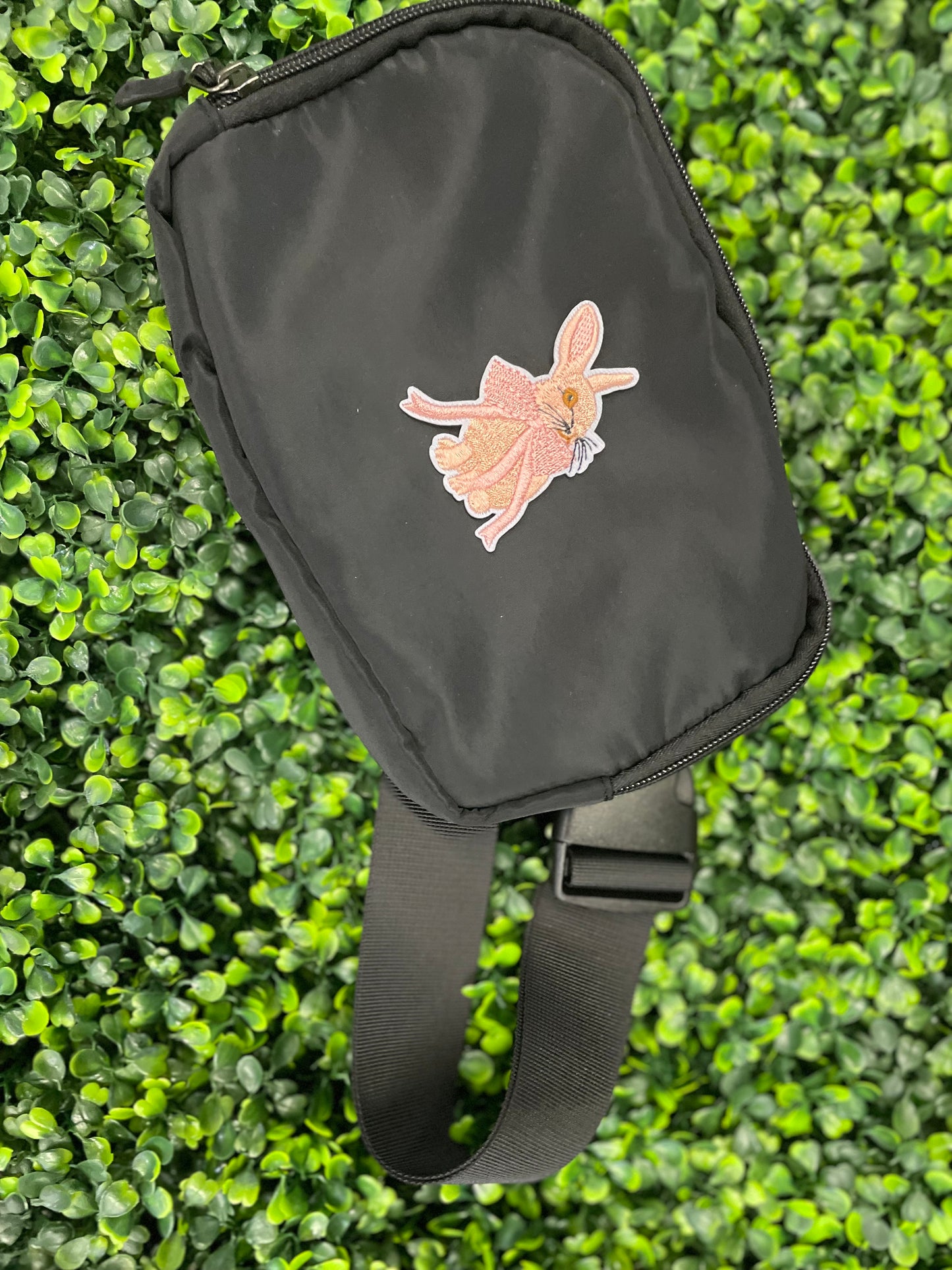 Embroidered patch of a pink bunny white a pink bow placed against a black shoulder bag
