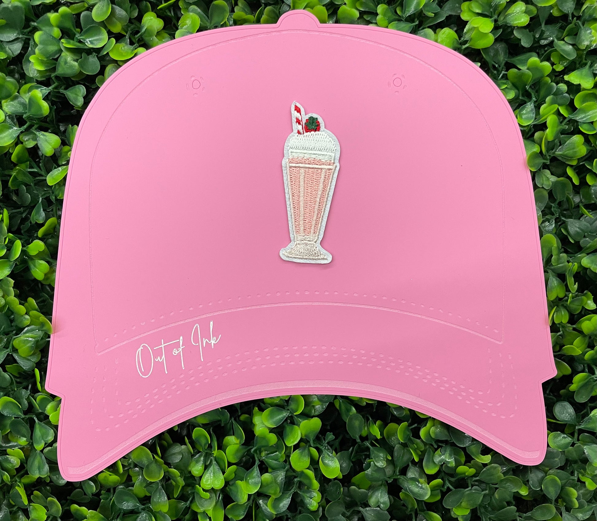 A pink milkshake embroidered patch with a cherry on top, held onto a pink hat