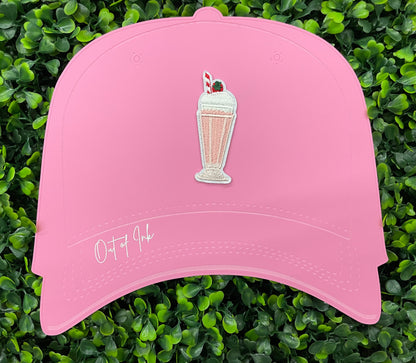 A pink milkshake embroidered patch with a cherry on top, held onto a pink hat