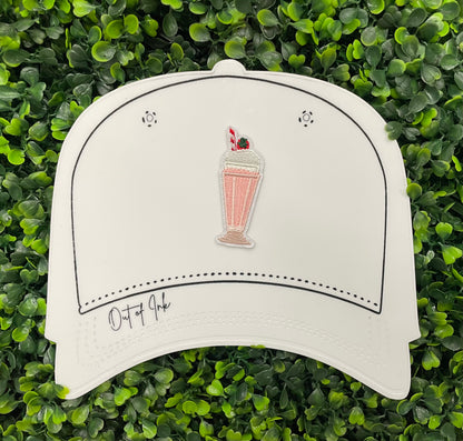 A pink milkshake embroidered patch with a cherry on top, held onto a white hat design 