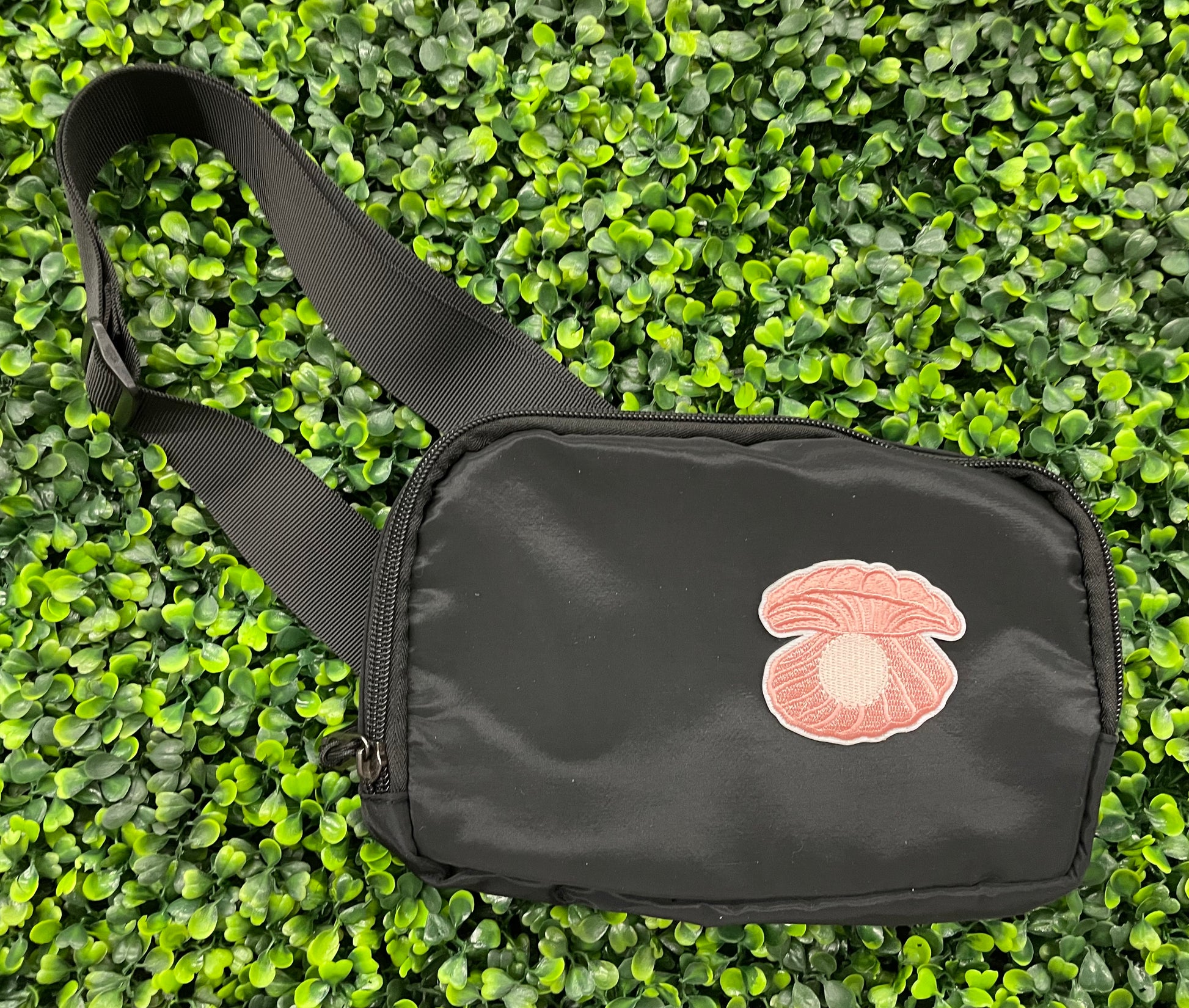A pink patch showcasing an embroidered design resembling an oyster shell with a pearl interior, held against a black bag 