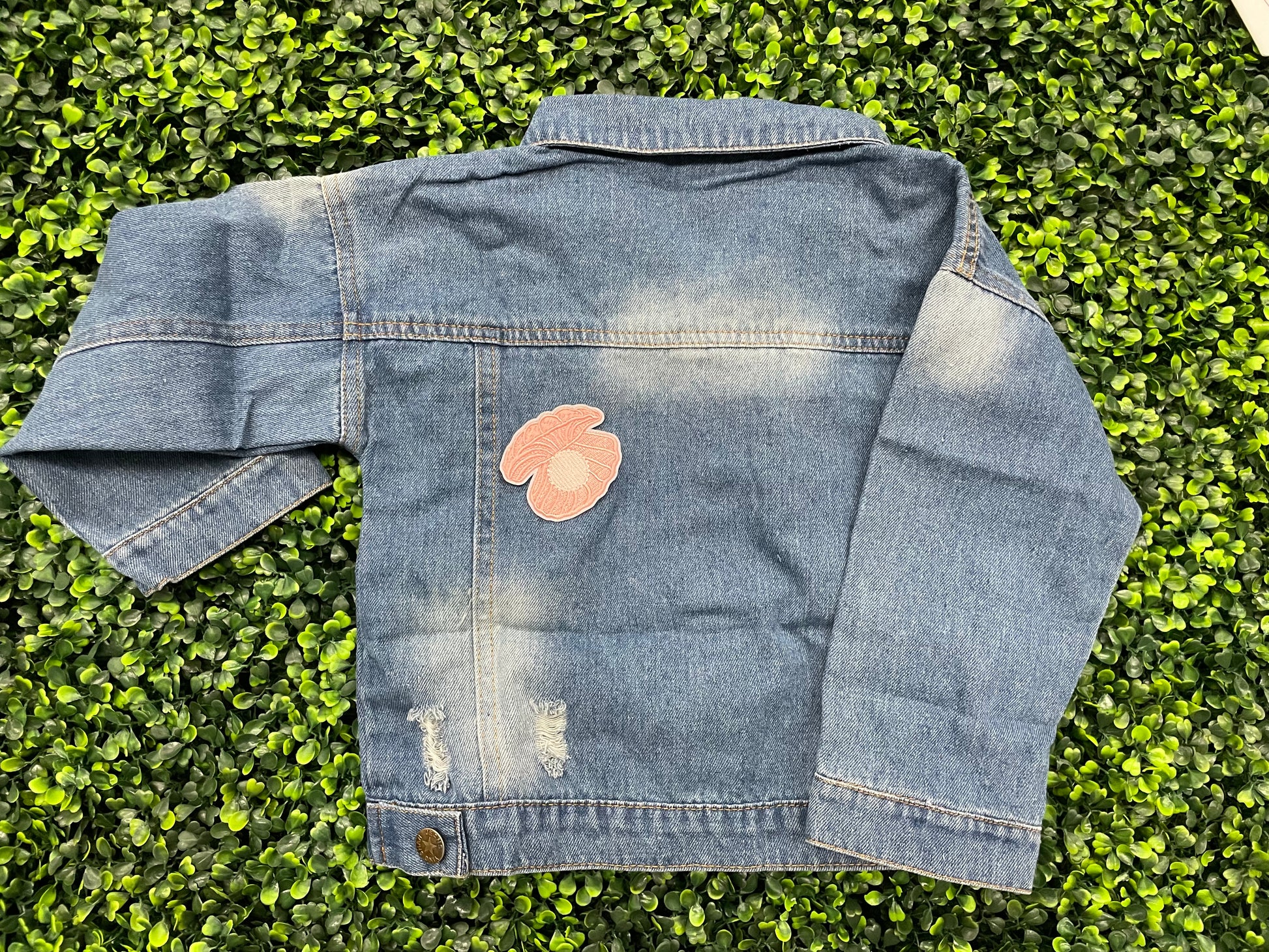 A pink patch showcasing an embroidered design resembling an oyster shell with a pearl interior, held onto a jean jacket
