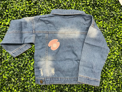 A pink patch showcasing an embroidered design resembling an oyster shell with a pearl interior, held onto a jean jacket