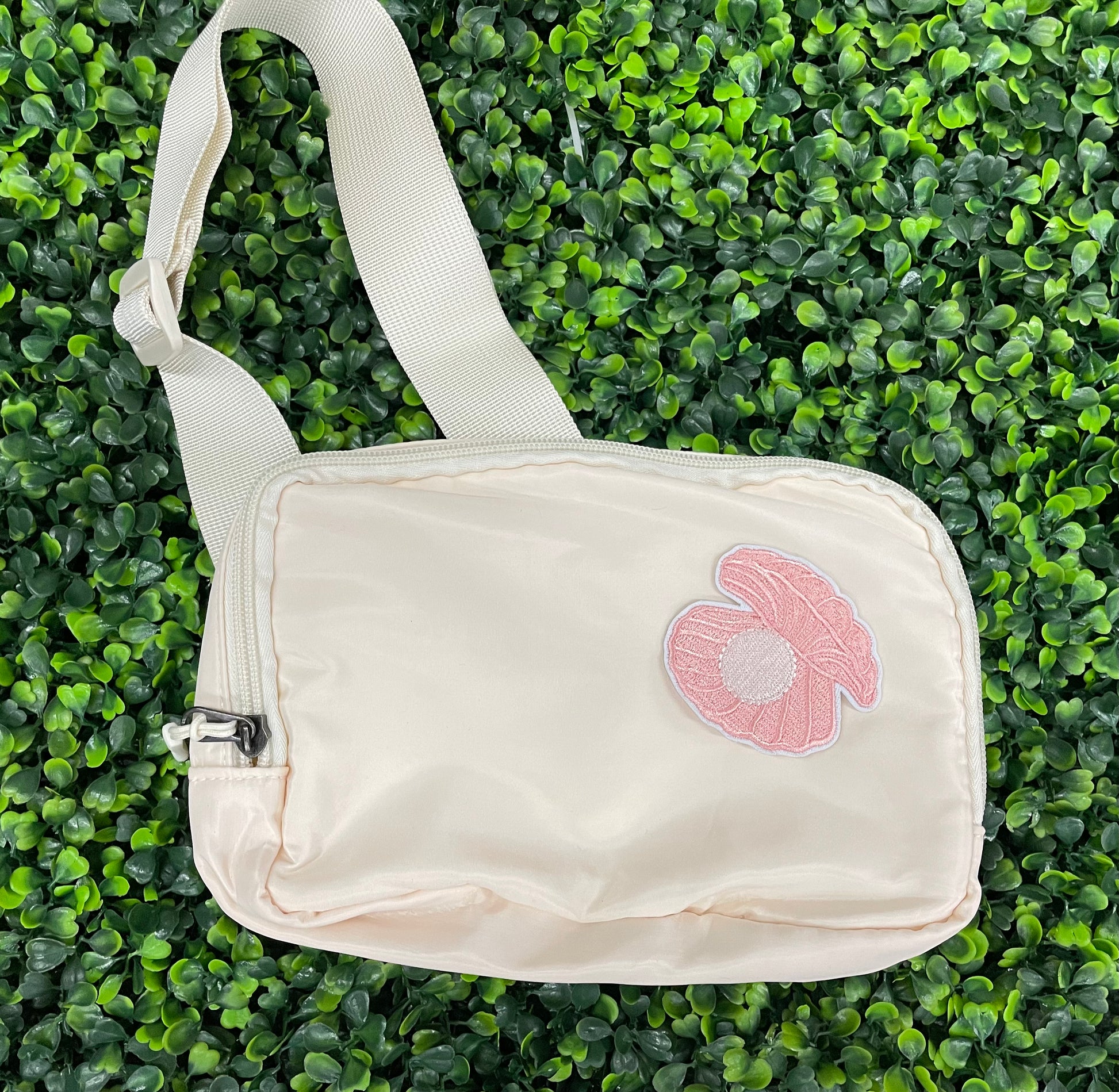 A pink patch showcasing an embroidered design resembling an oyster shell with a pearl interior, held agaist a green leafy background