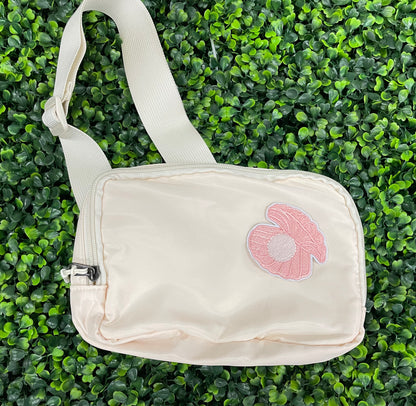 A pink patch showcasing an embroidered design resembling an oyster shell with a pearl interior, held agaist a green leafy background
