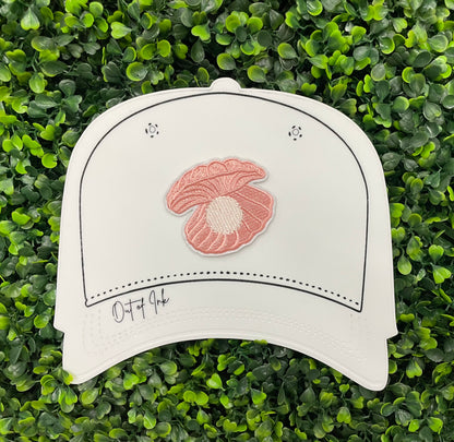 A pink patch showcasing an embroidered design resembling an oyster shell with a pearl interior, held against a white hat