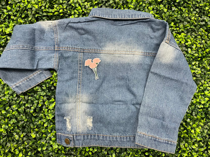 A hand holding an iron-on patch with embroidered pink roses attached to a green stem, set on a jean jacket