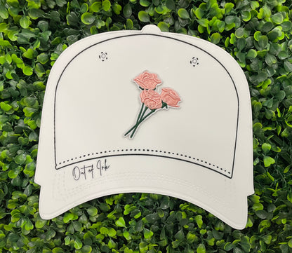 A hand holding an iron-on patch with embroidered pink roses attached to a green stem, set on a white hat