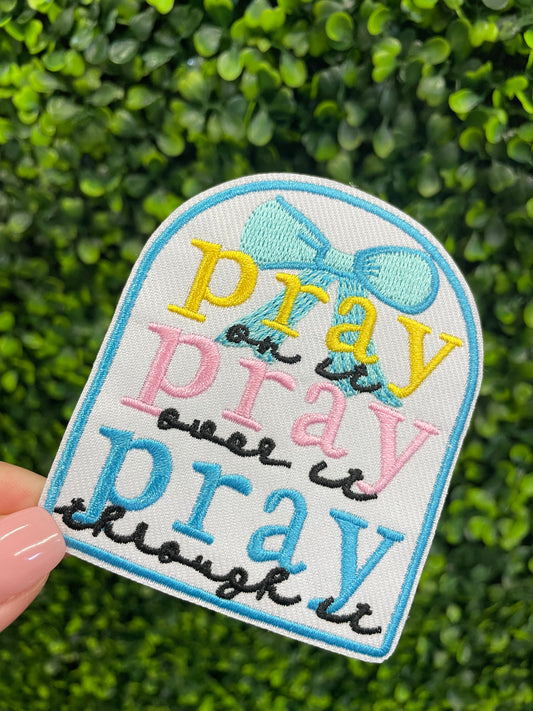 Embroidered patch with 'pray on it, pray over it, pray through it' text in various colors held against a green background